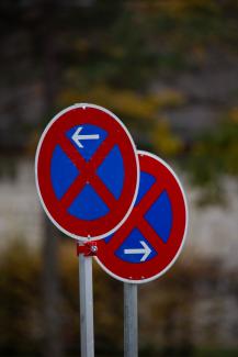 Two red and blue no parking traffic signs outdoors with arrows pointing left and right.