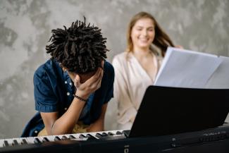 Young boy feeling overwhelmed at piano lesson with supportive teacher nearby