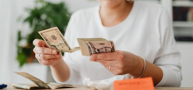 A woman sits indoors counting cash at her office desk, focusing on finances.